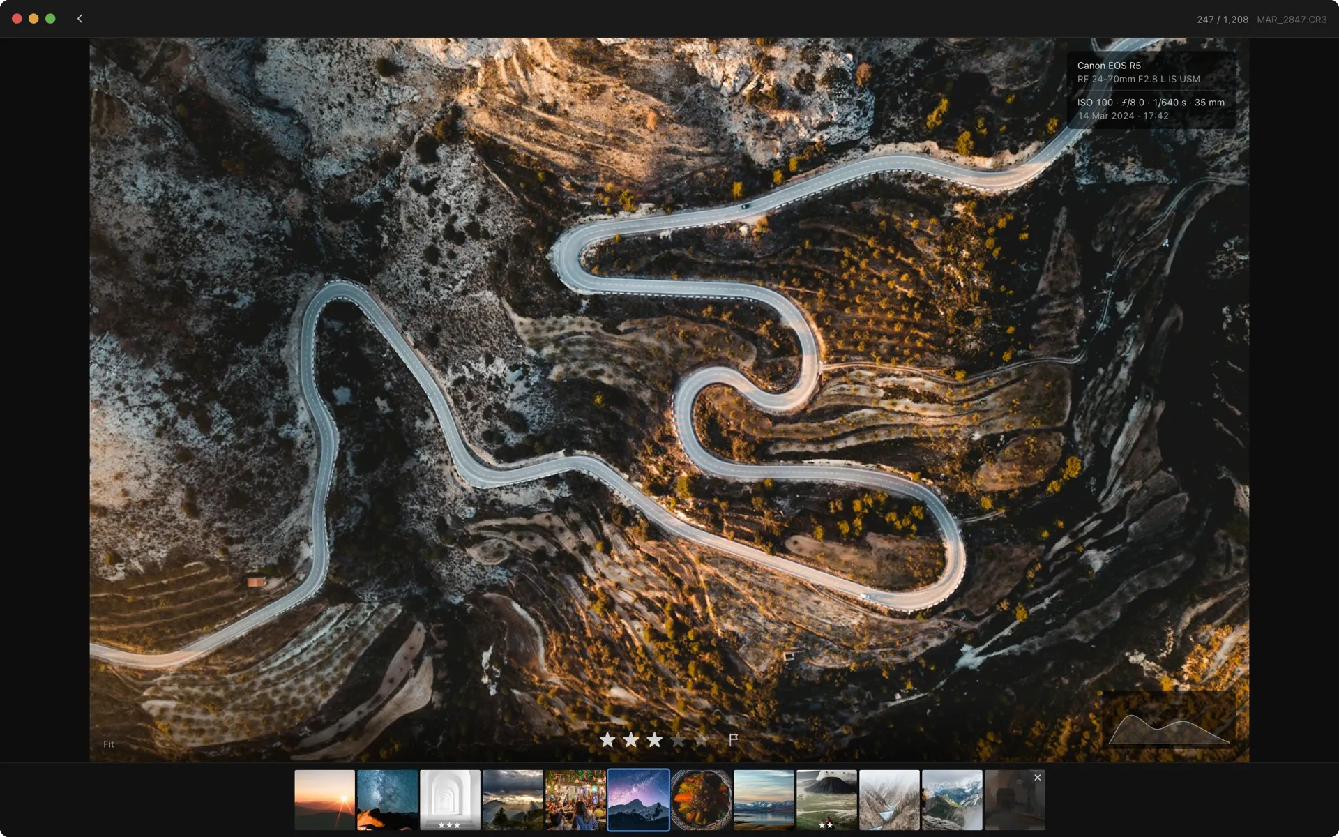 Negativo's loupe view: an aerial shot of a switchback mountain road filling the screen, with the star rating and pick flag centred below it, a filmstrip of the surrounding frames along the bottom, and the camera settings tucked into the top corner.